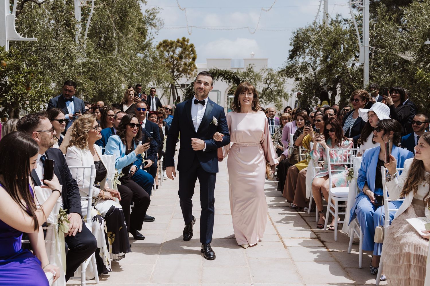 Wedding ceremony outdoors with guests seated along an aisle.