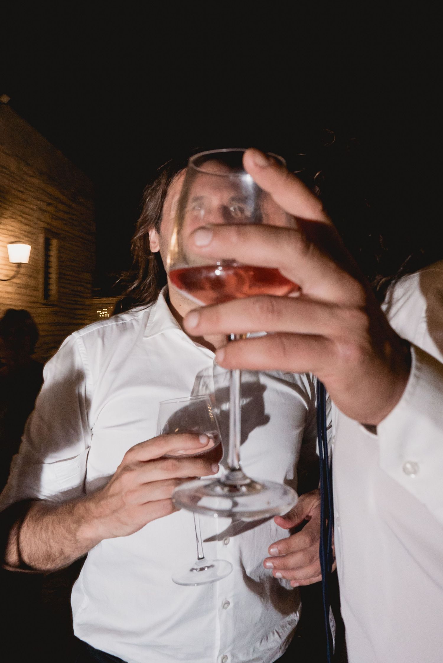 People toasting with wine glasses in a dimly lit setting at a celebration event.