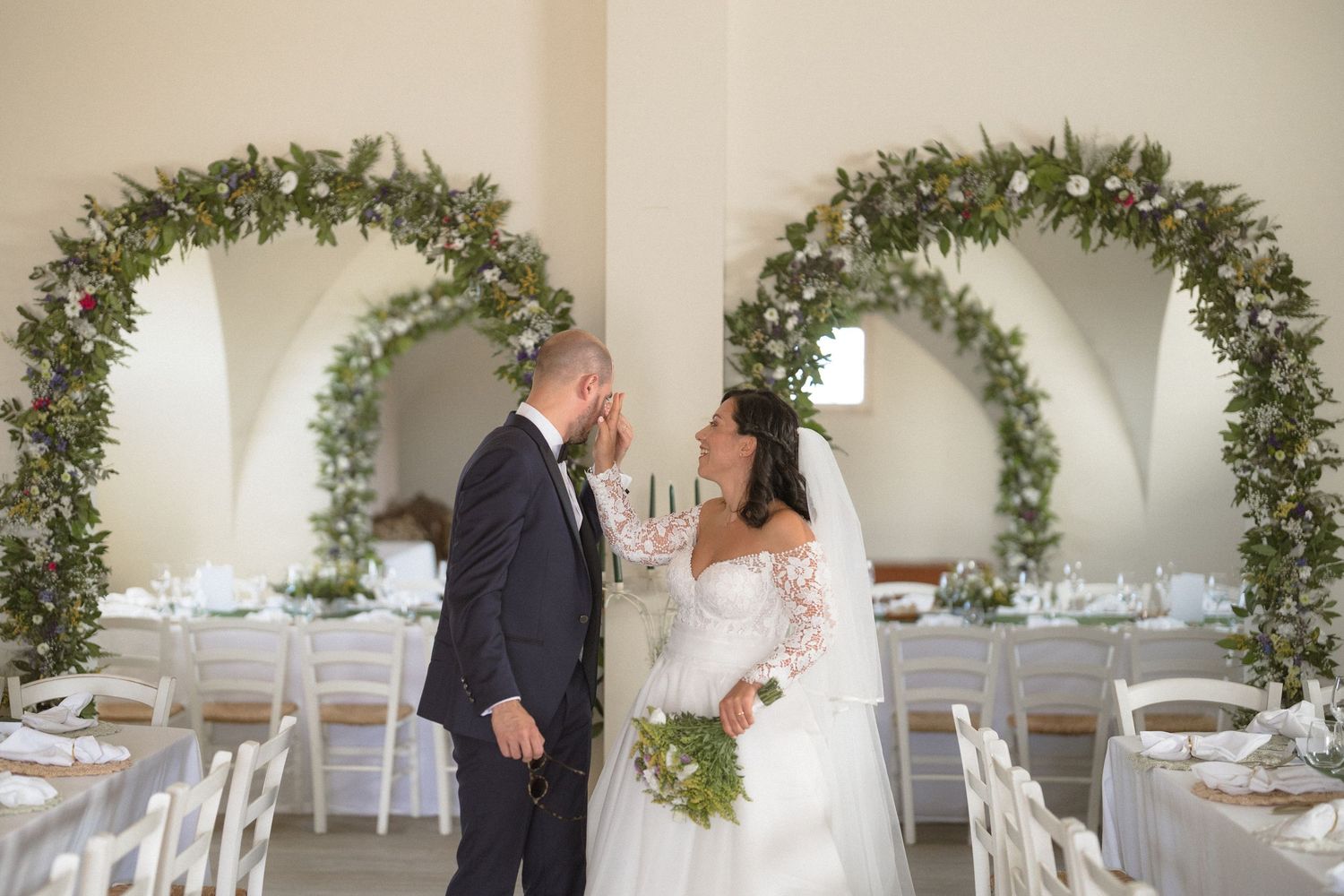 White wedding reception venue decorated with elegant greenery arches and table settings.
