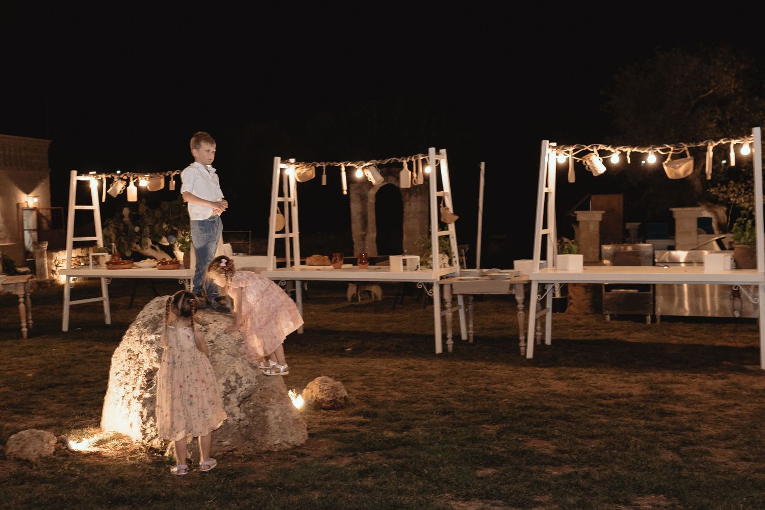 Outdoor wedding reception setup at night with string lights illuminating tables and chairs under a dark sky.