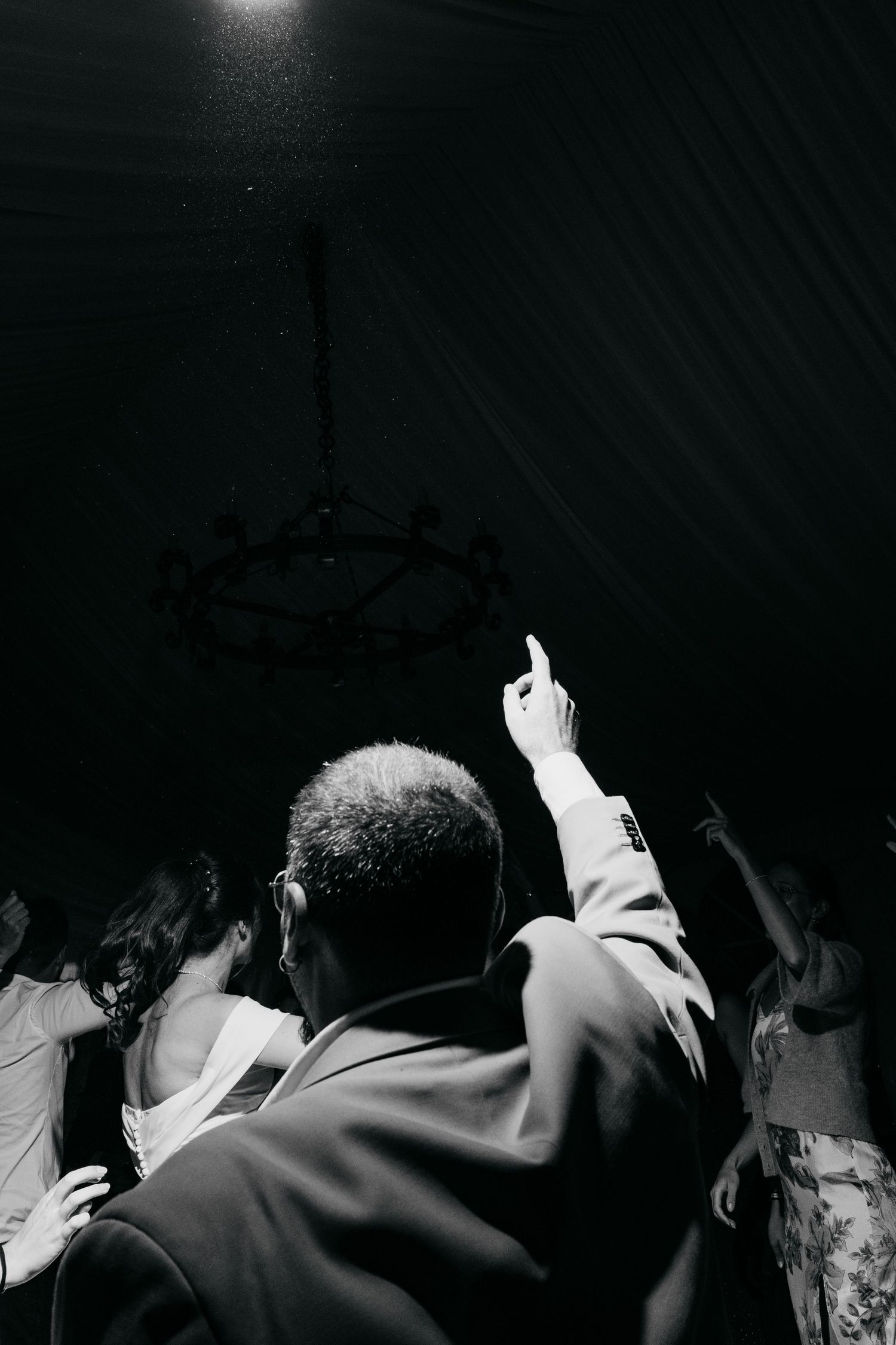 A silhouetted figure points upward at a light fixture during a dark event.