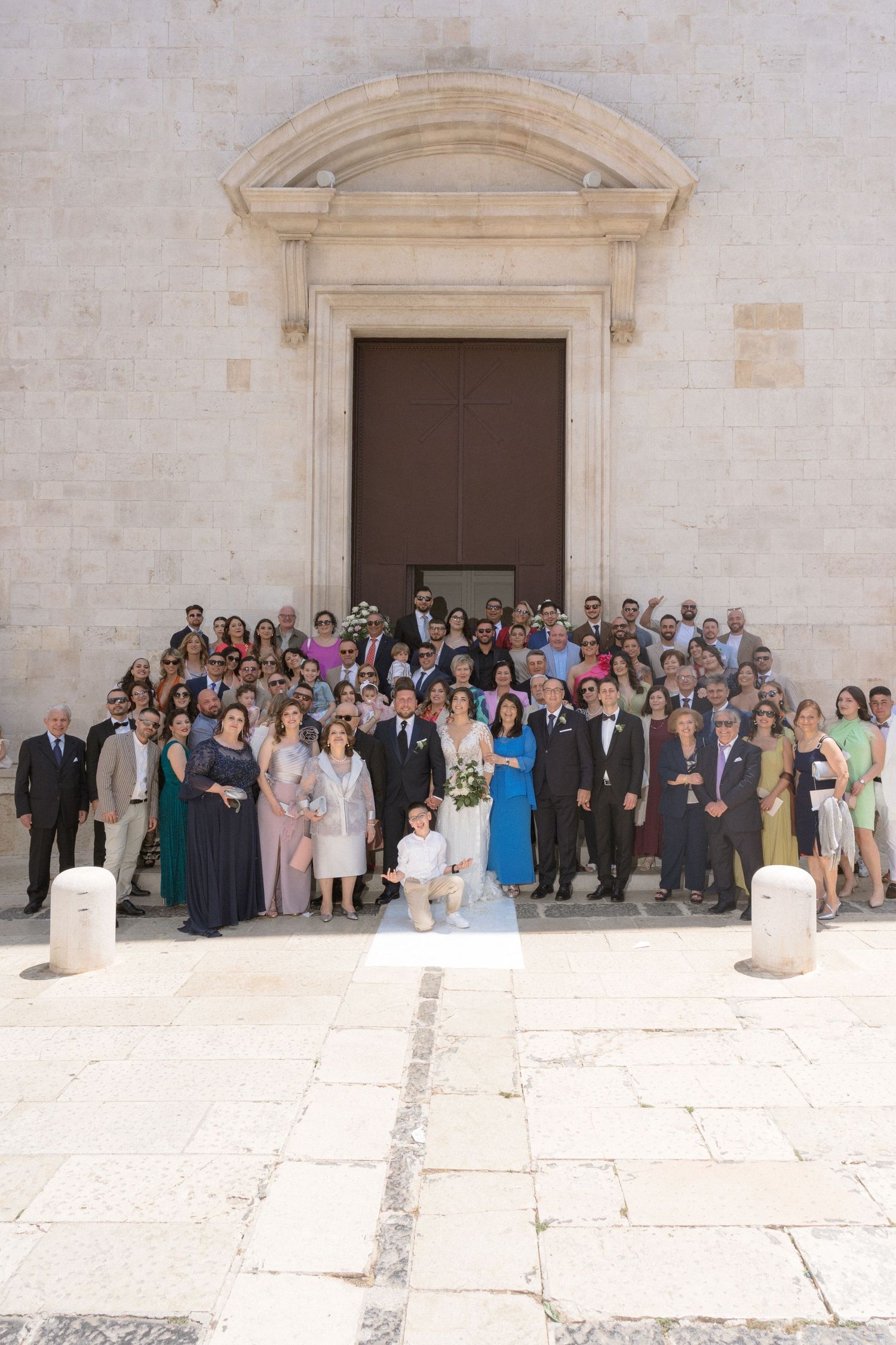 Large group wedding photo of guests gathered outside a stone church building.