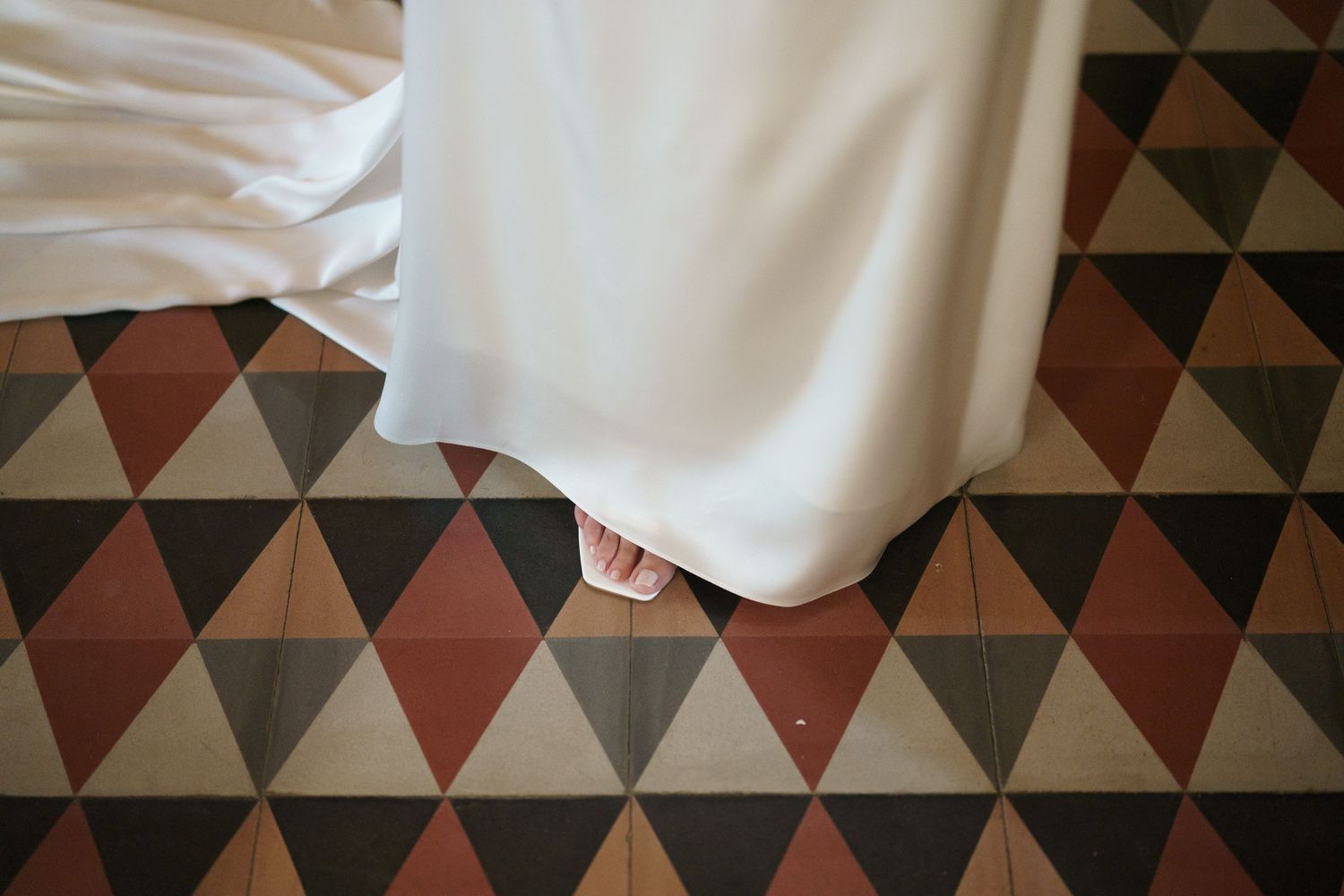 White fabric drapes over vintage geometric floor tiles in red, black and grey patterns.