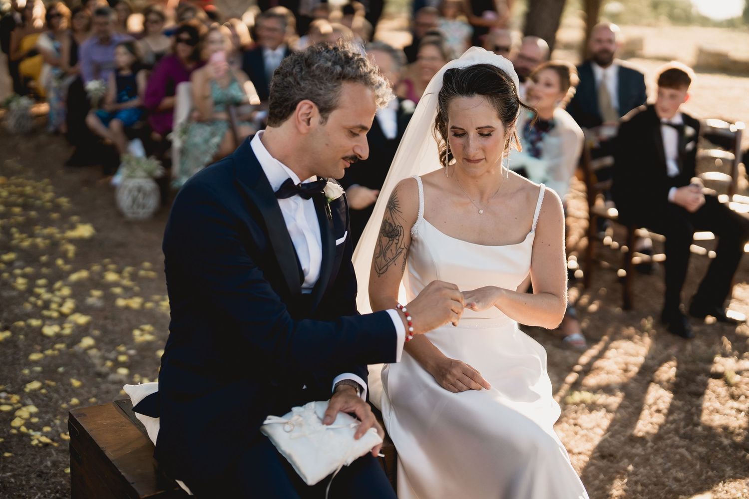 A bride and groom share an intimate moment during their outdoor autumn wedding ceremony with guests seated behind them.