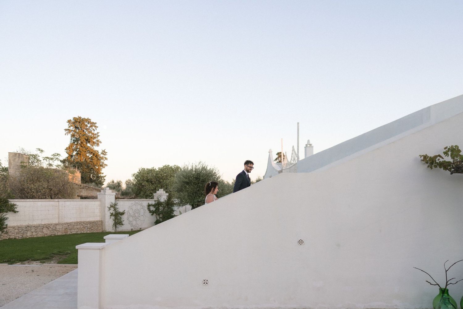 Bride and groom walking up white steps at a sunny outdoor Mediterranean wedding venue.