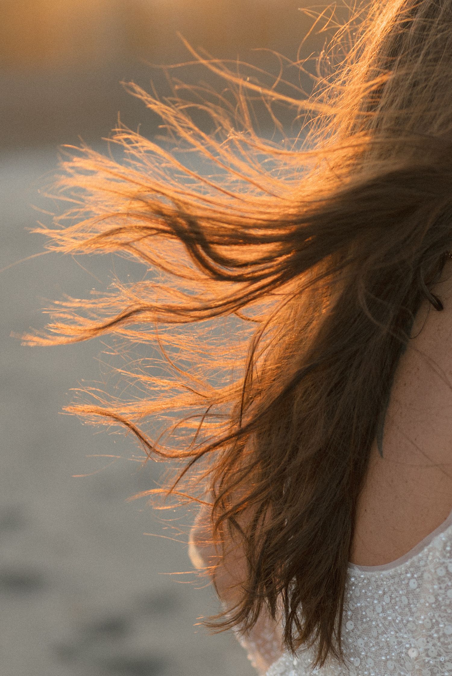 Sunlit hair blowing in the wind against sunset light, showing sparkly dress detail.
