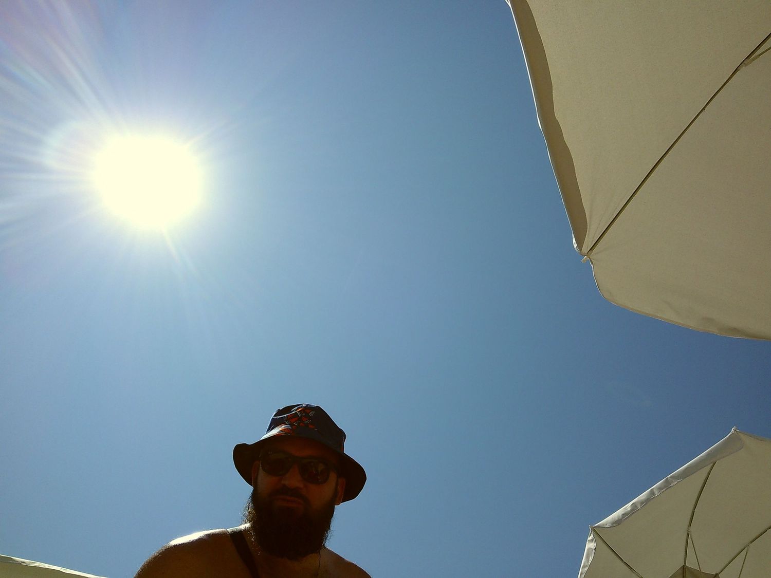 A sunny beach day viewed from under a beach umbrella with bright blue sky overhead.