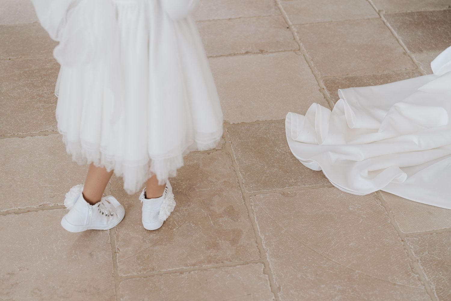 White wedding dress hem and comfortable bridal sneakers on a tiled floor.