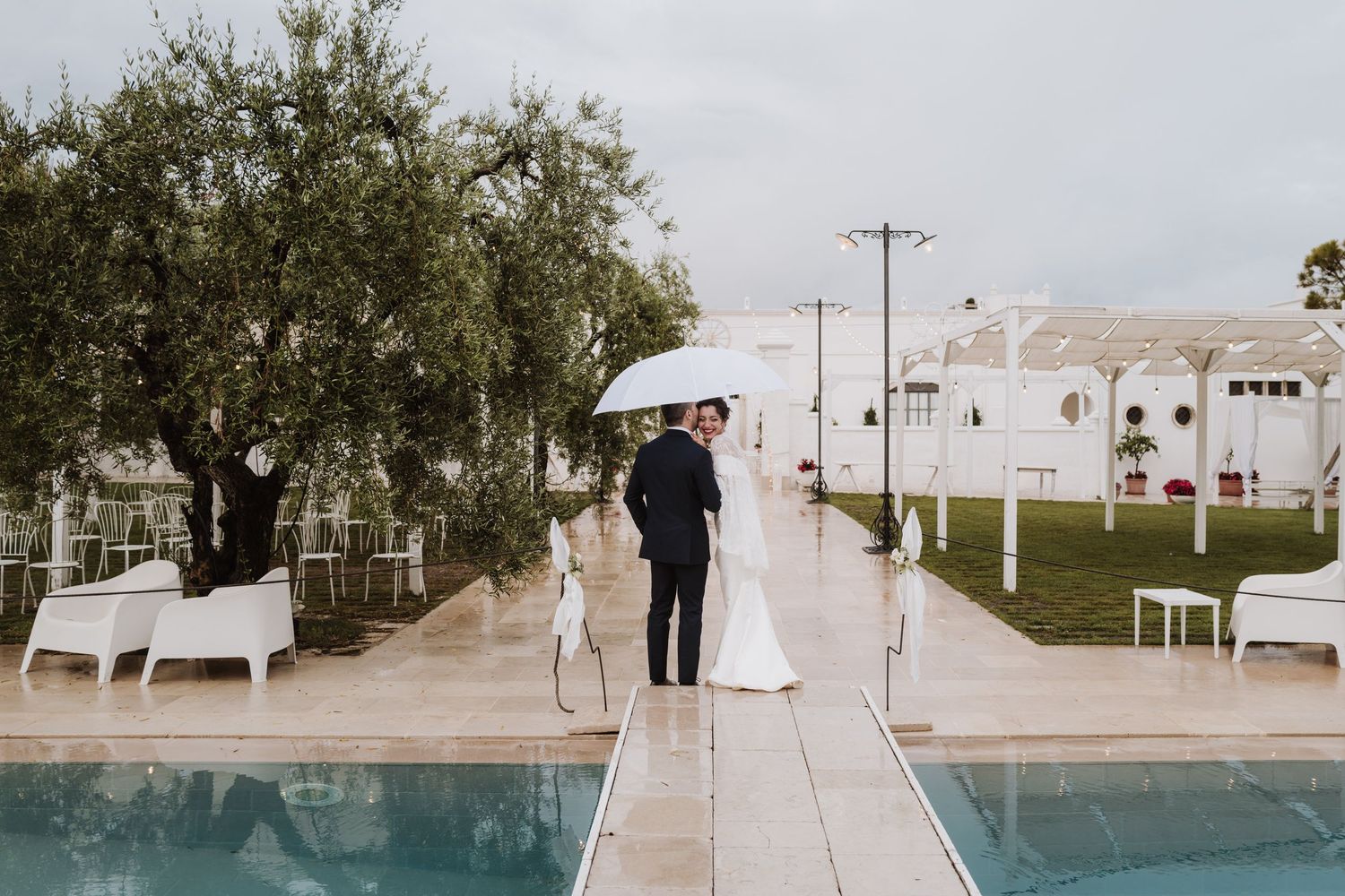 Wedding couple walking along poolside path at outdoor venue.