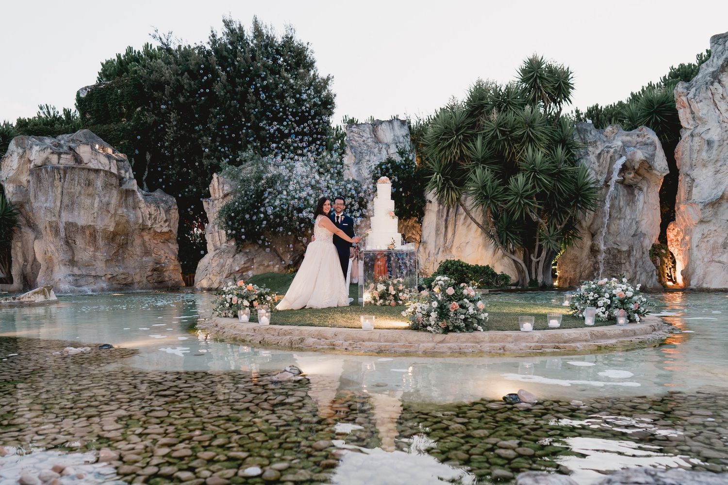 A wedding ceremony setup with floral arrangements against dramatic rock formations near a reflective pond.