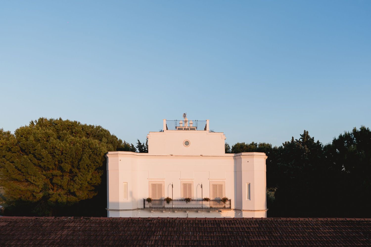 Minimalist pink Mediterranean wedding venue captured at dusk against trees.