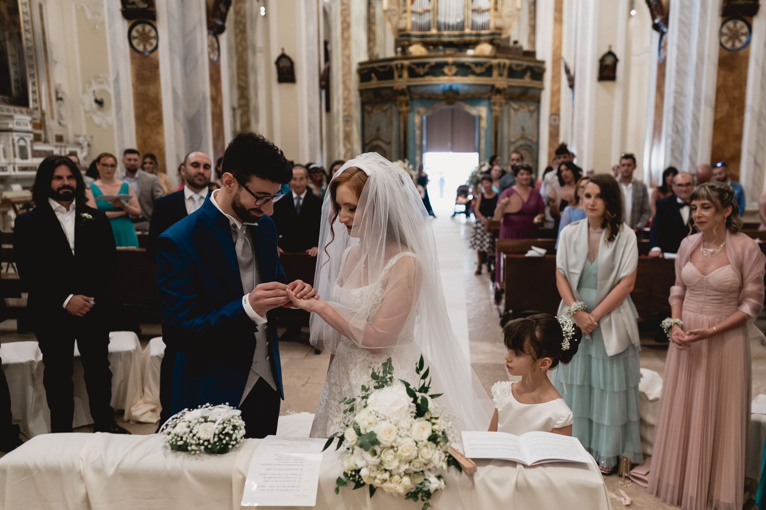 Traditional church wedding ceremony with couple signing marriage documents at decorated altar table.