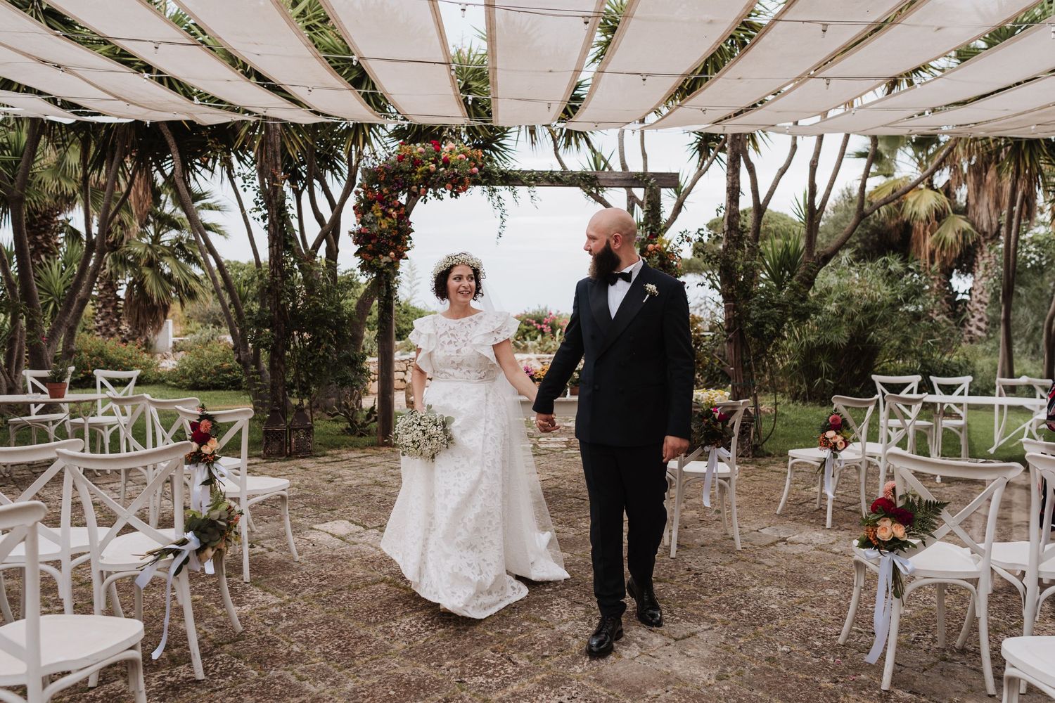 Newlyweds stand together under draped canopy at garden wedding venue.