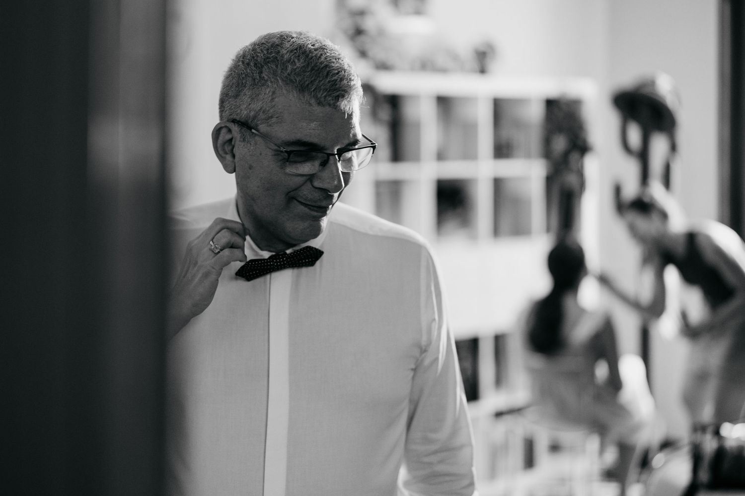 A person in a white dress shirt and bow tie adjusts their collar in a monochrome candid shot.