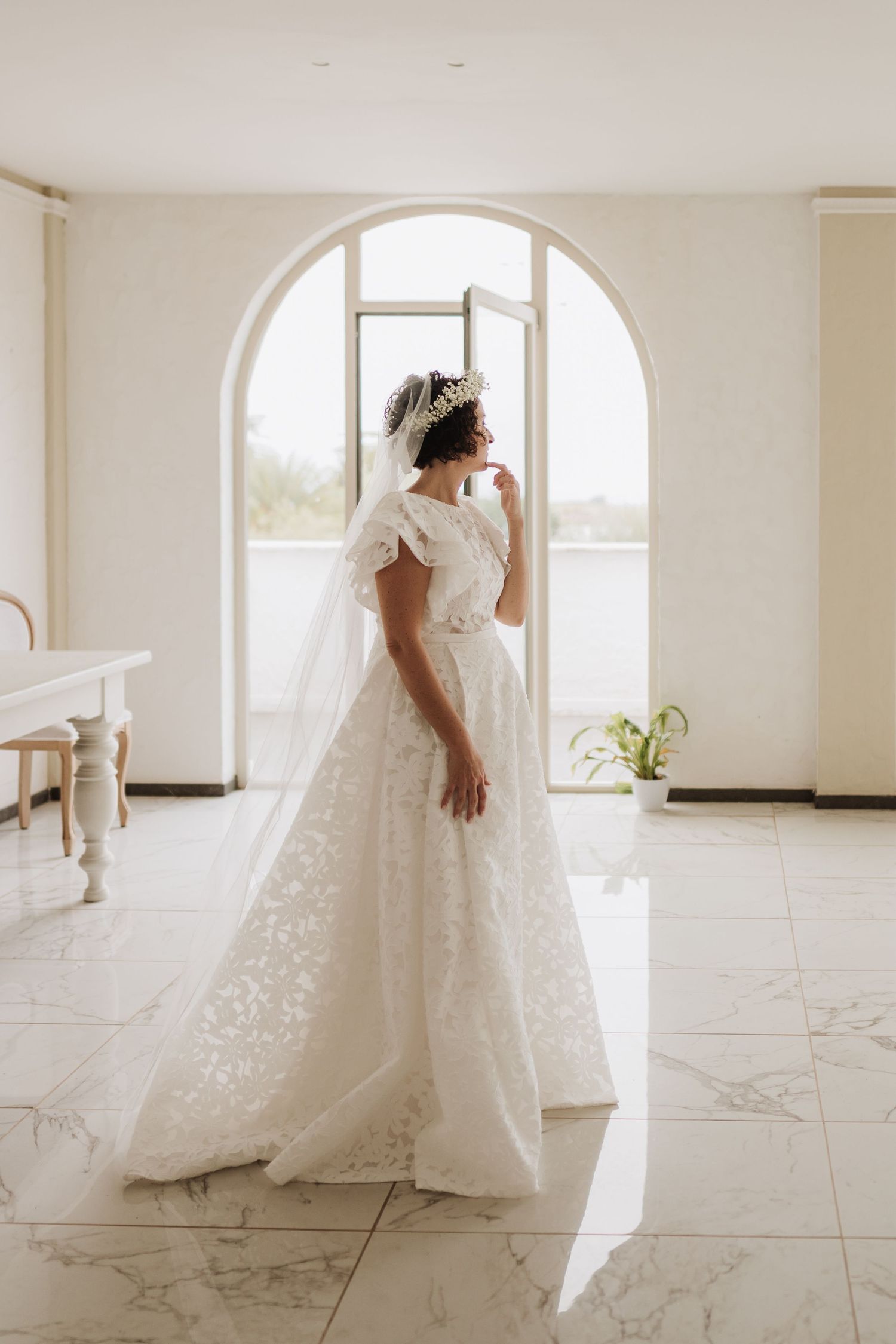 Full-length view of a wedding gown in front of an arched window with natural light.