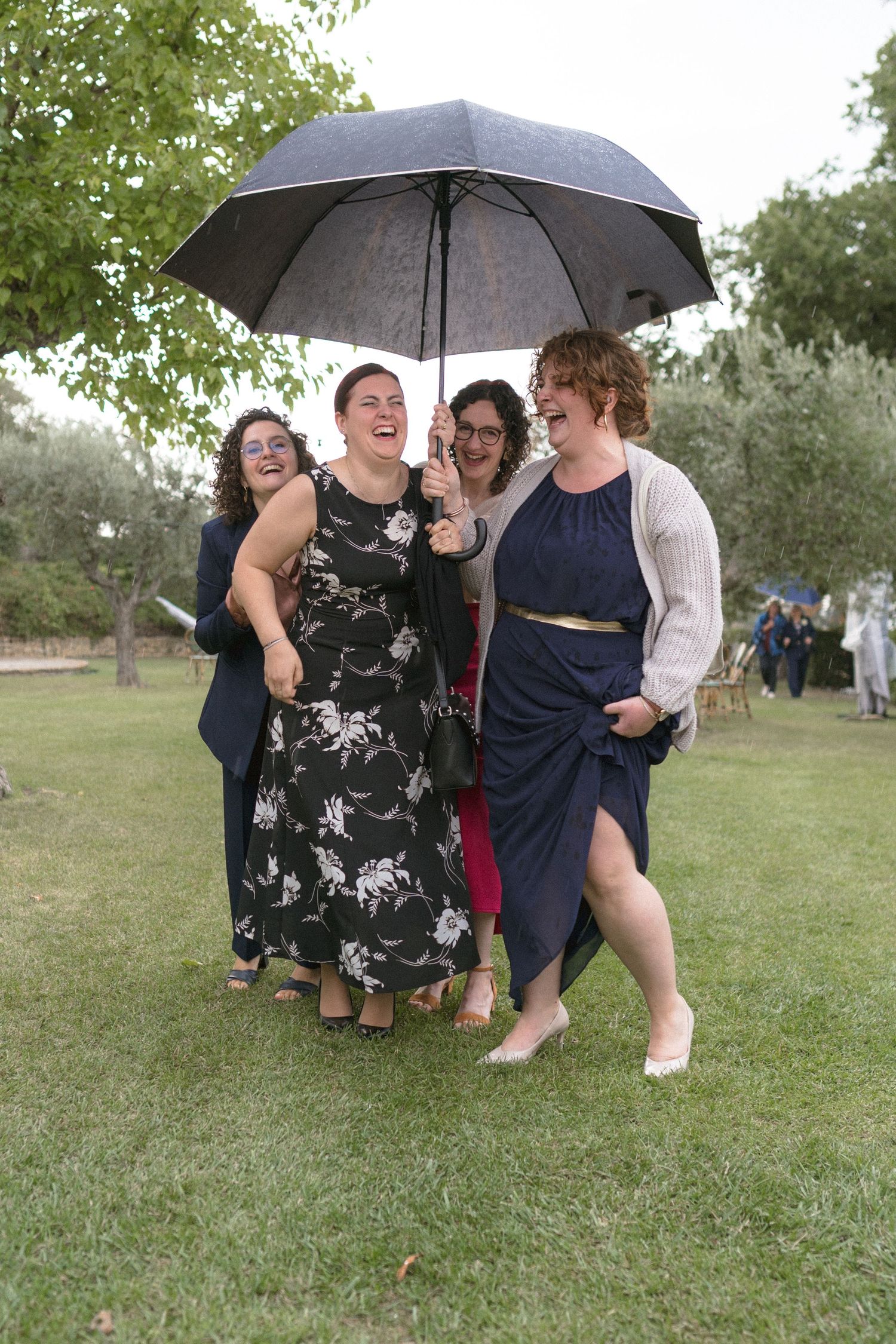 Wedding guests laughing and sheltering under umbrellas on a rainy day.