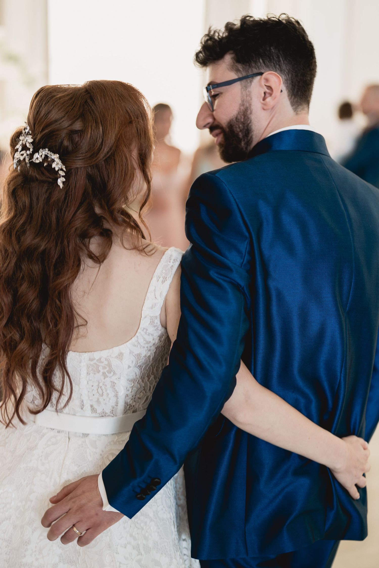 A couple shares an intimate moment at their wedding, with the bride in white and groom in navy blue suit.