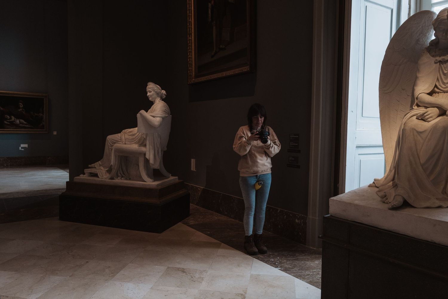 Museum visitor photographs classical statues in an art gallery.