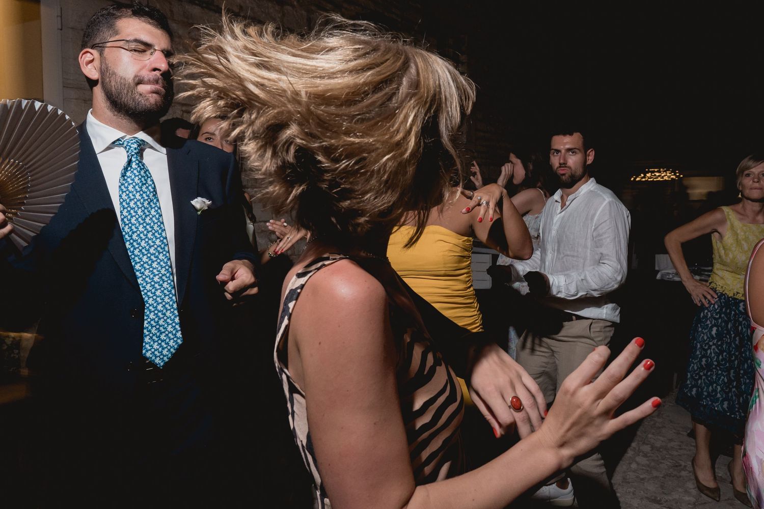 People dancing energetically at a party, with blonde hair flying through the air on a dark dance floor.