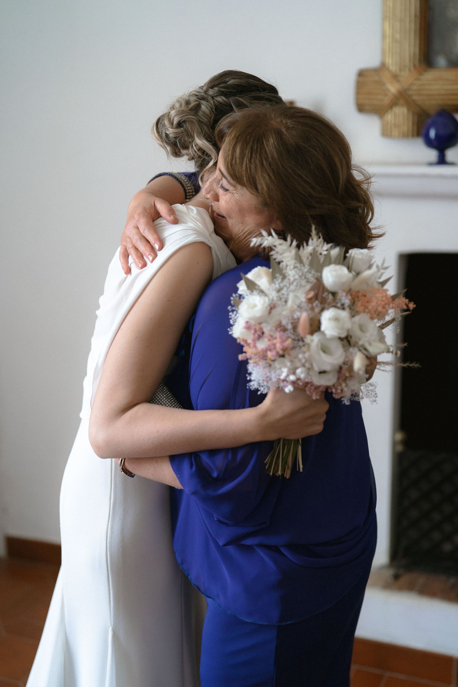 Emotional embrace between two people in formal attire with white flowers at an indoor event.
