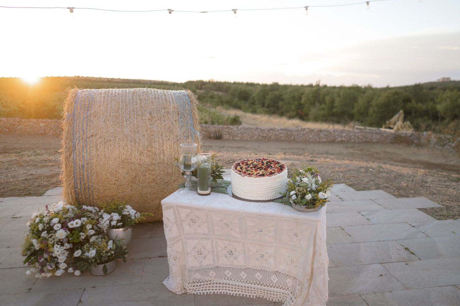 Rustic outdoor wedding venue setting at sunset with hay bale seating and floral decorations.