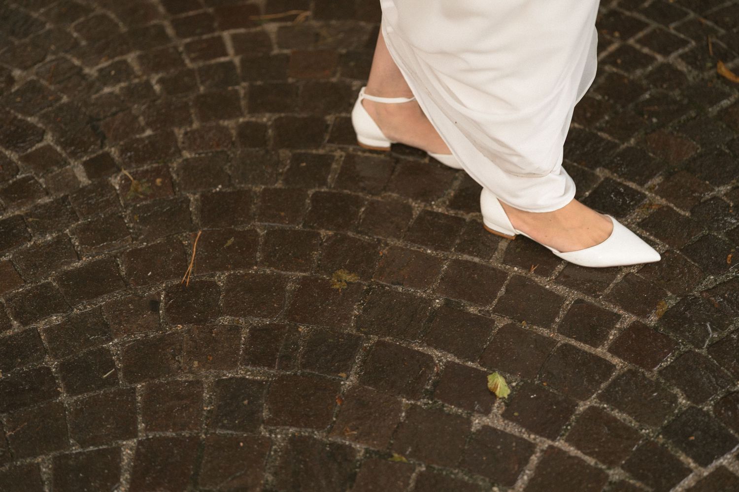 Close-up view of white bridal shoes on a cobblestone path.