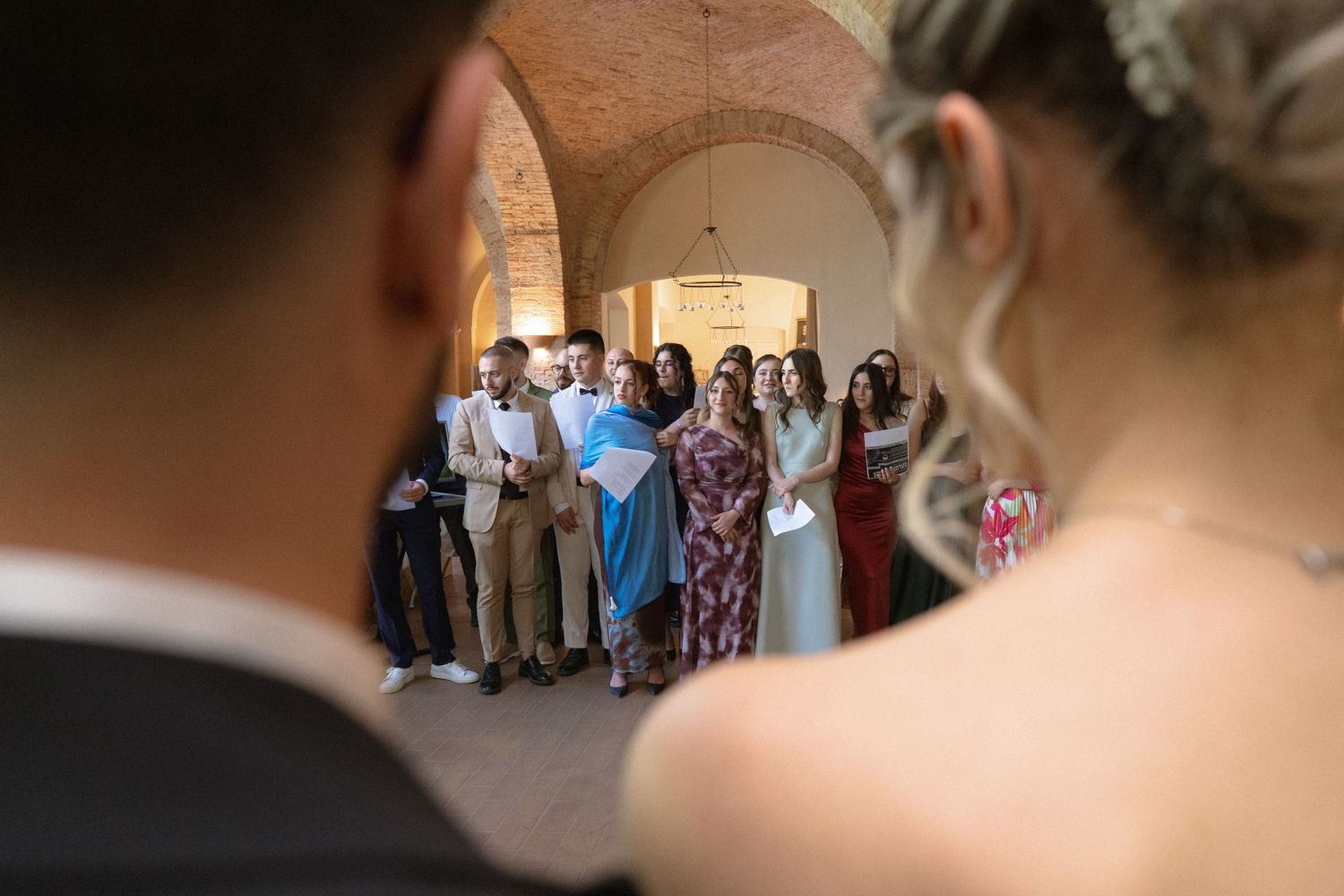 Wedding guests gathered in a sunlit brick courtyard watching ceremony proceedings.