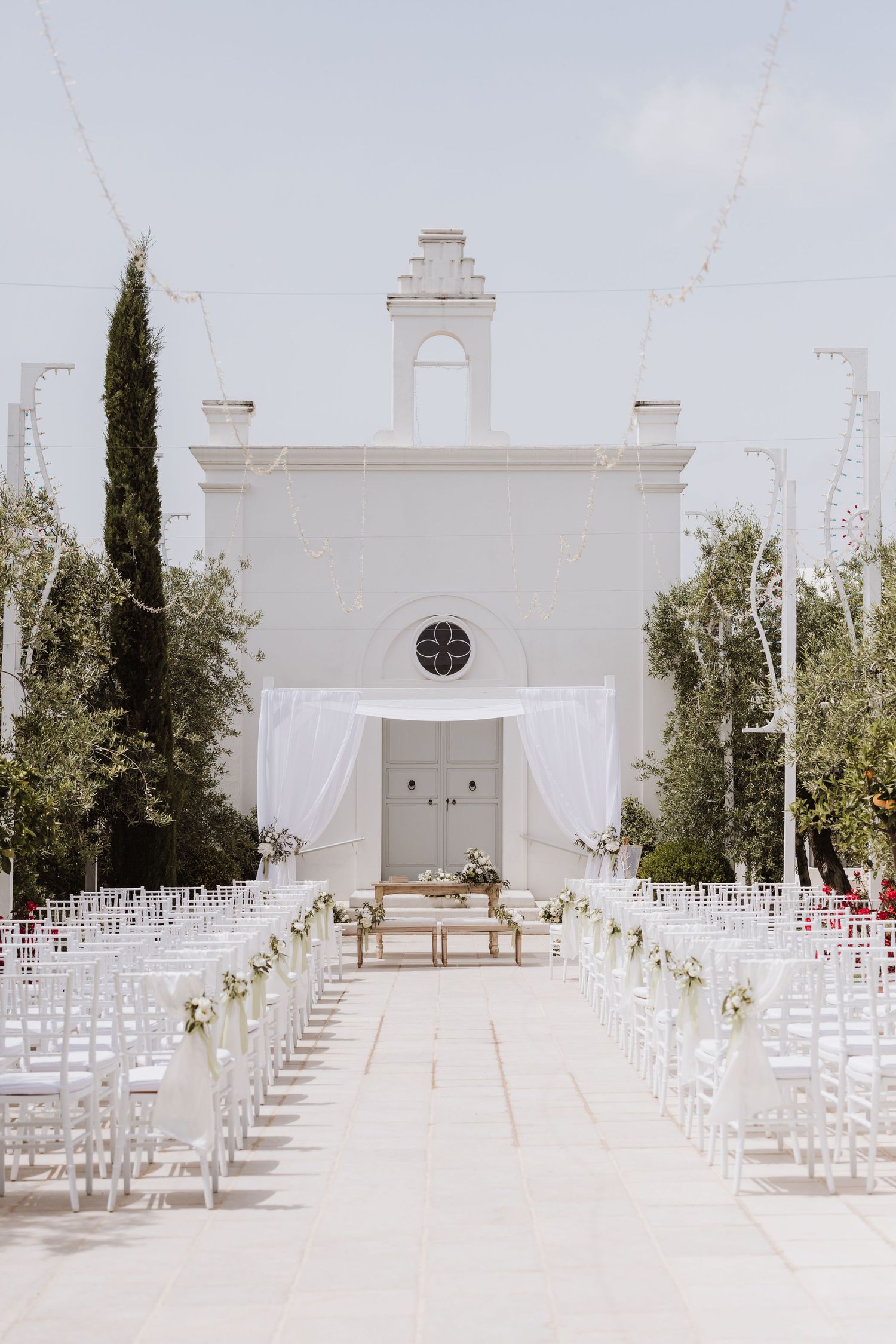 White chapel wedding venue with rows of chairs lined up along an aisle decorated with flowers.
