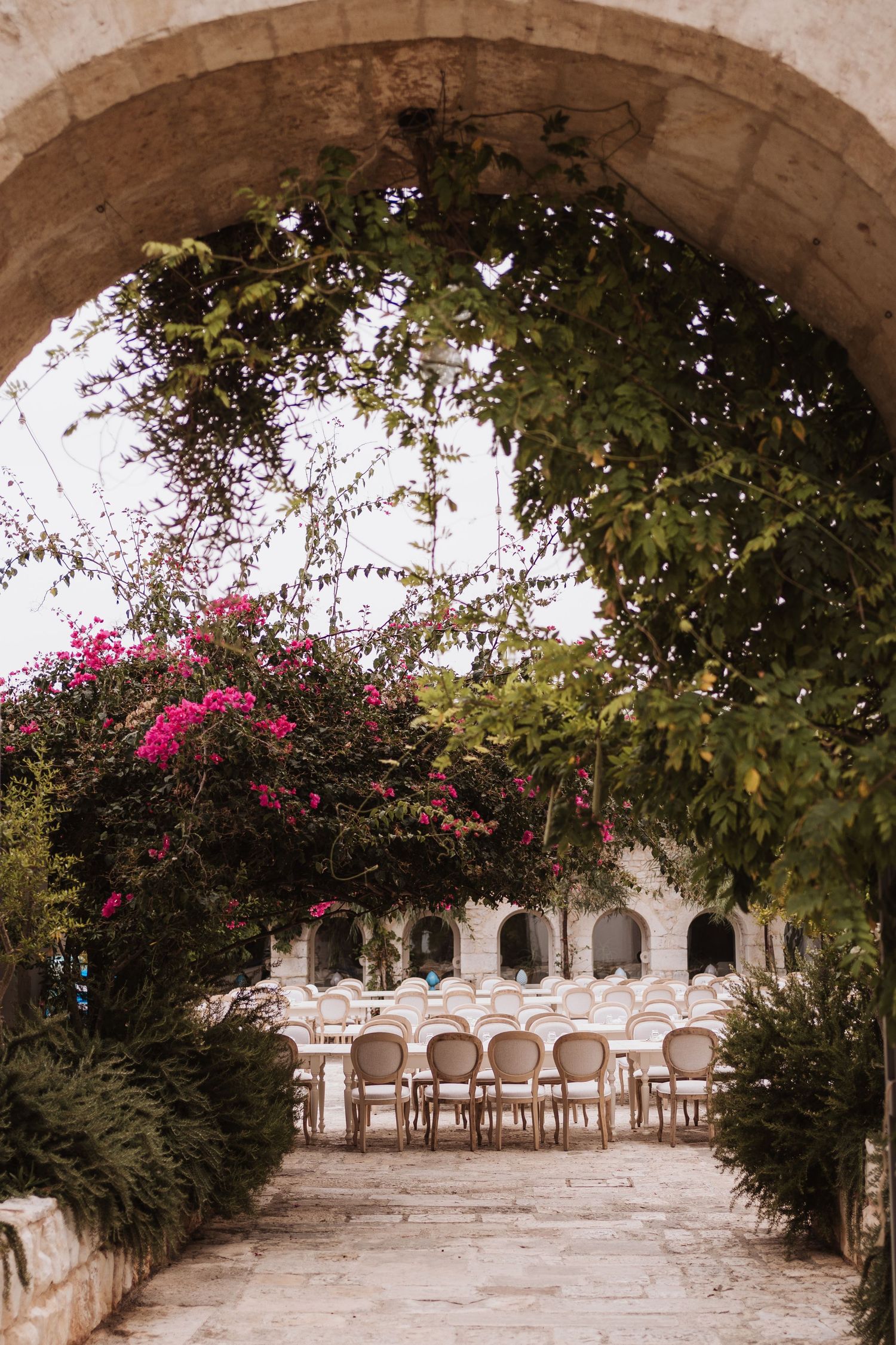 An elegant stone archway leads to a garden reception area with white chairs and tables.