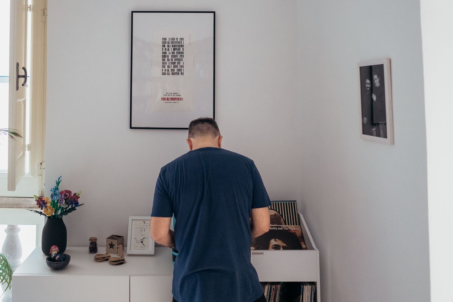 A person in a navy blue t-shirt stands facing a wall with framed artwork.
