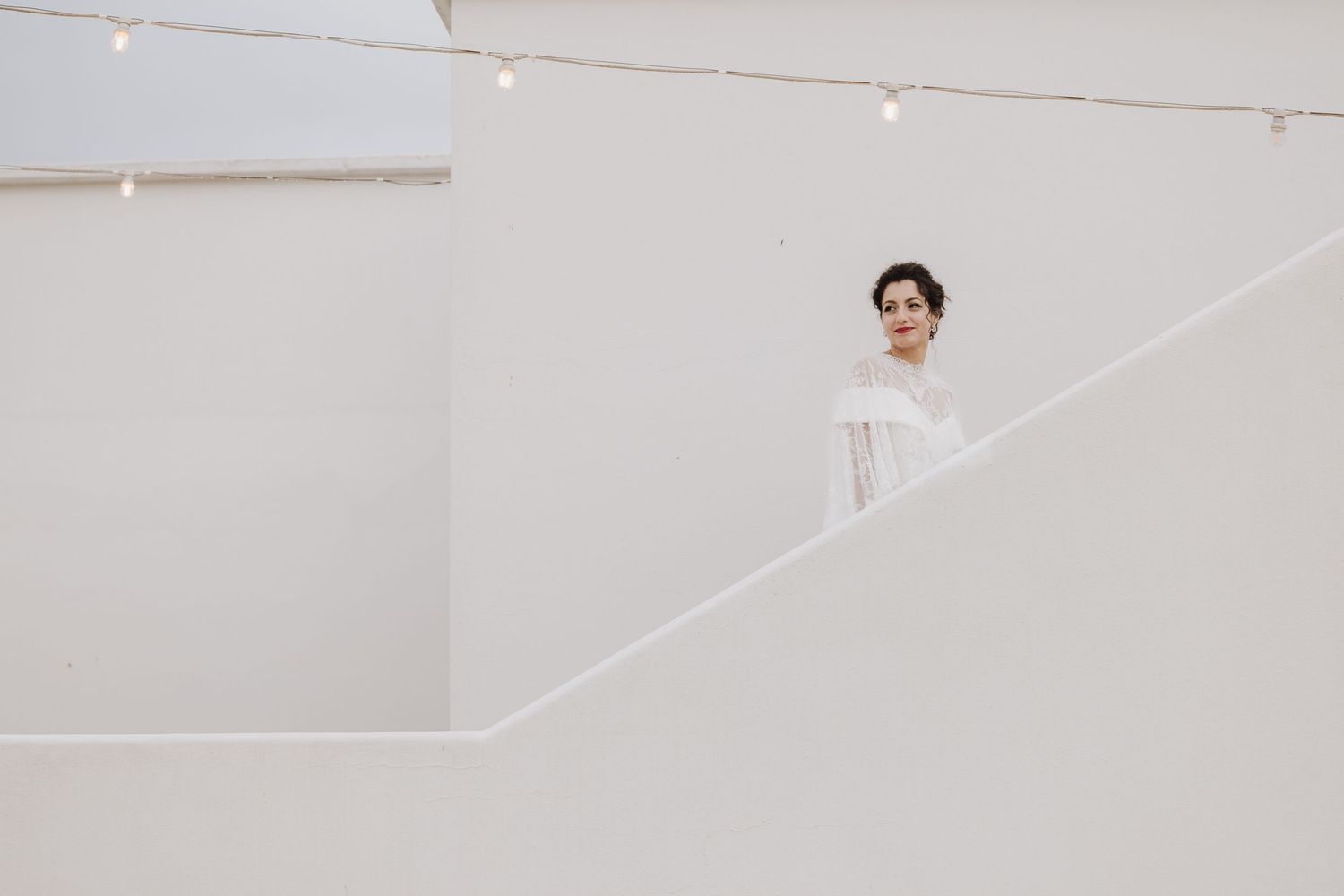Figure stands on a white minimalist staircase wearing light colored clothing in a clean architectural setting.