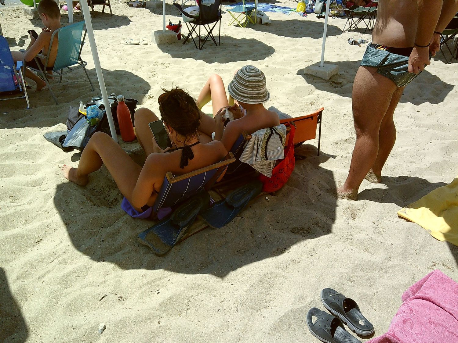 Beach goers relaxing on lounge chairs under umbrellas on a sandy beach.