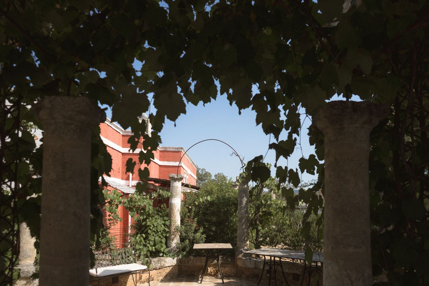 Stone archways frame a sunny Mediterranean courtyard with red-roofed buildings in the background.
