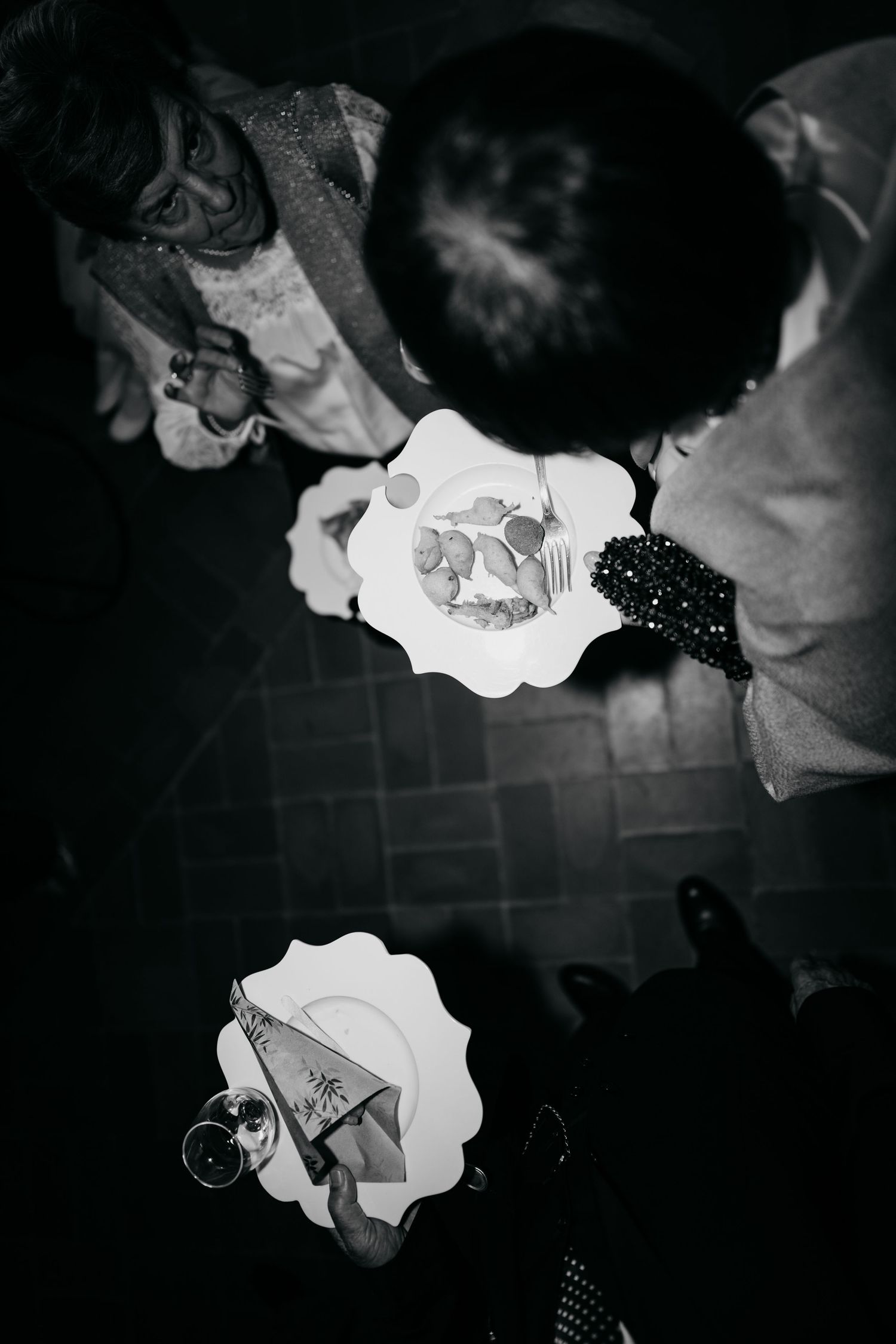 Black and white aerial view of wedding guests holding plates of food at a reception gathering.