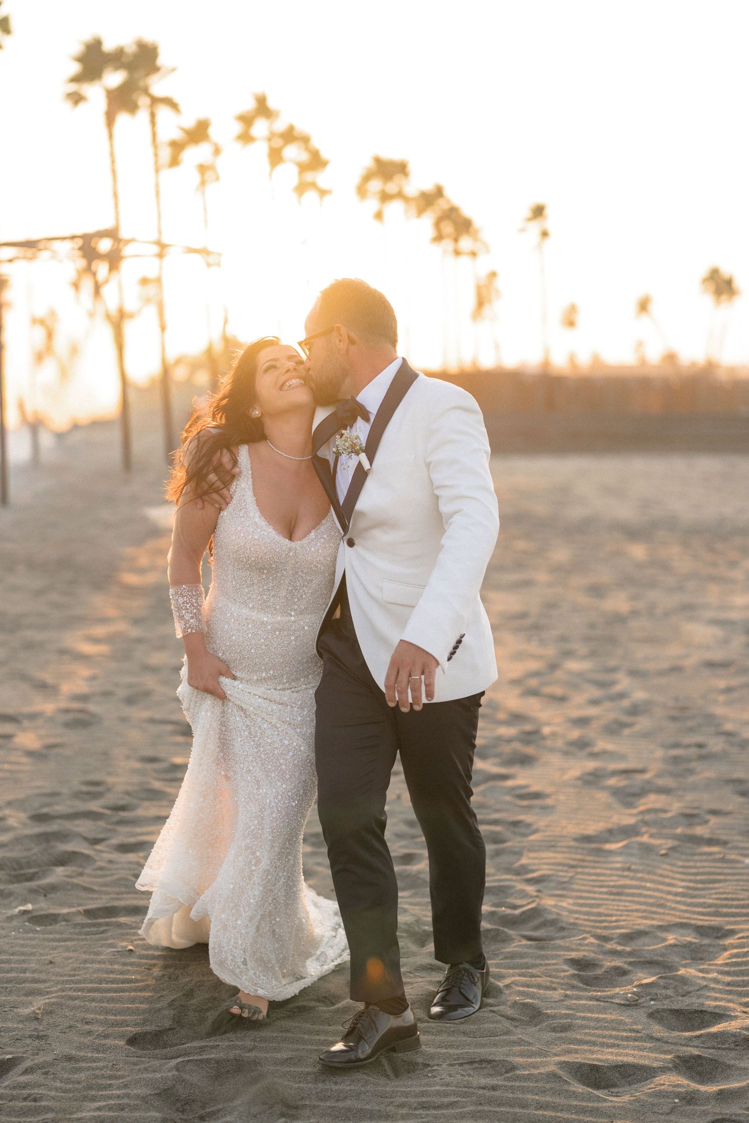 A romantic beach wedding photo of a couple embracing at golden hour with palm trees in the background.