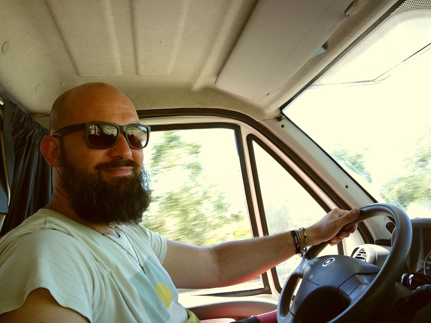 A person wearing sunglasses drives a vehicle on a sunny day.