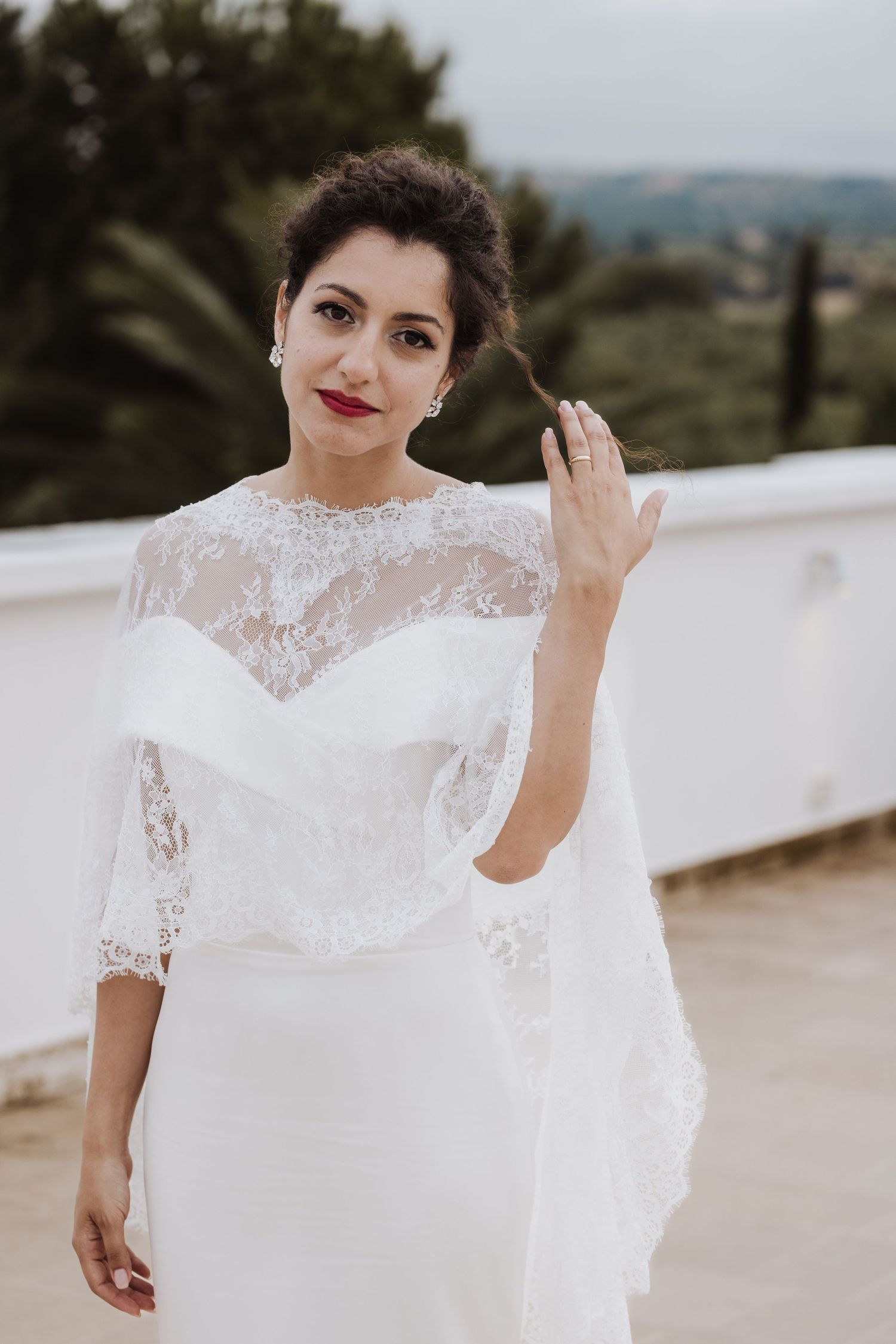 Stylish bridal portrait featuring a white lace wedding dress against an outdoor backdrop.