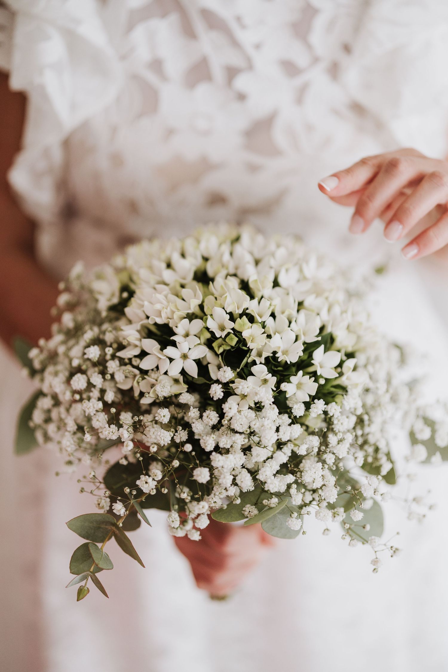 A delicate bouquet of white baby's breath flowers and eucalyptus leaves held against a white dress.