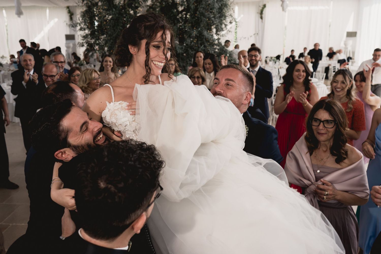 Group lifts the bride during an energetic dance celebration at a wedding reception.