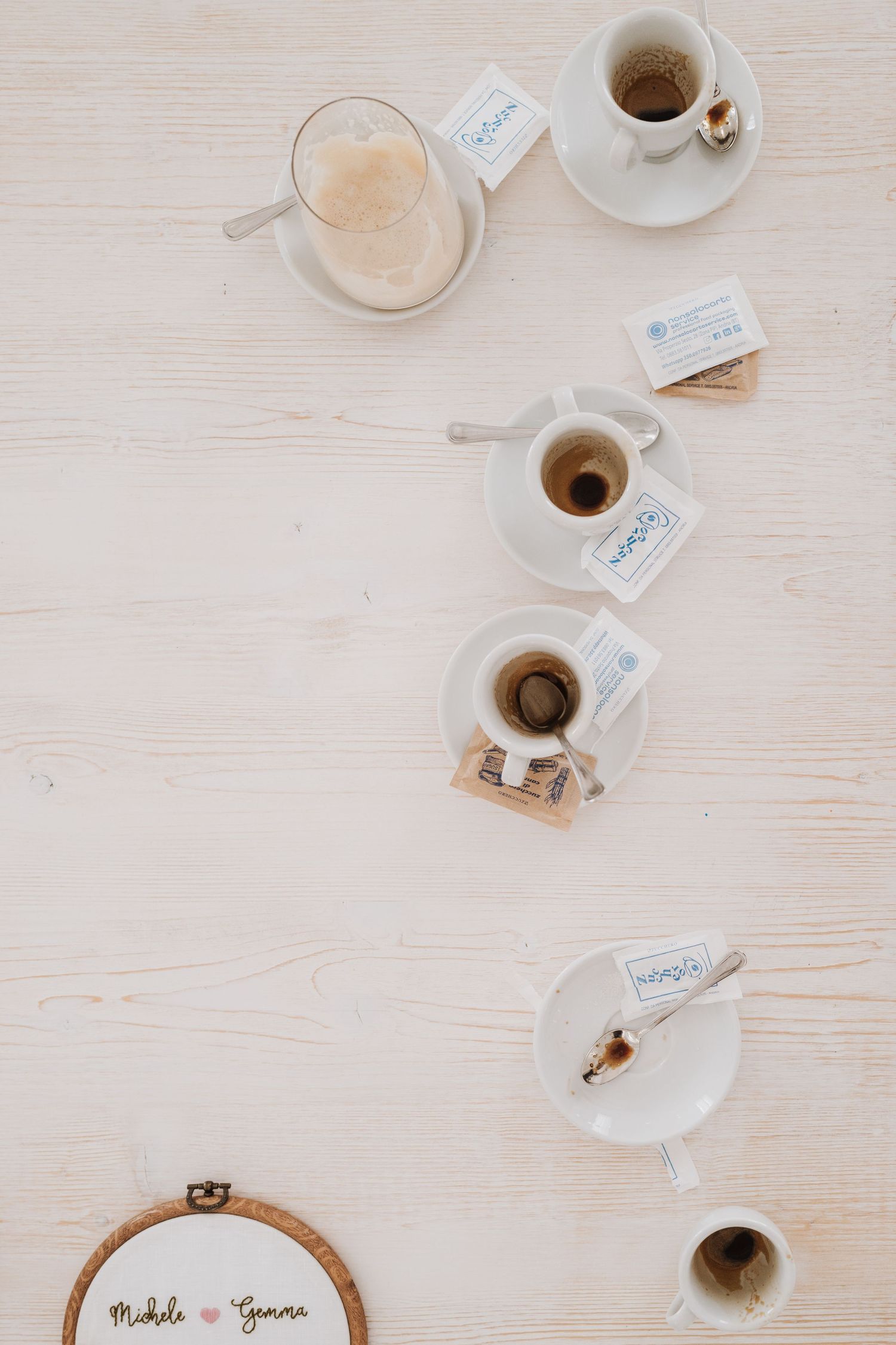 Overhead view of coffee cups and tea settings arranged on a white surface with embroidery hoop.