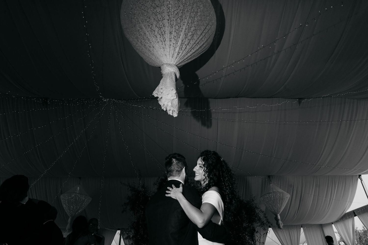 Black and white photo of couple dancing under paper lantern at reception.