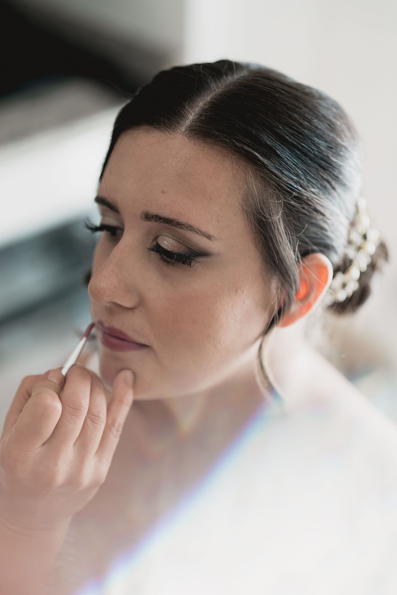 Makeup artist applying lipstick to a bride during wedding preparations.
