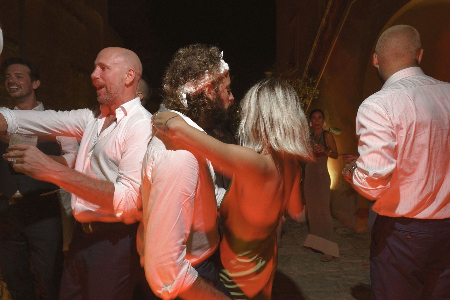Wedding guests dancing and celebrating in a dimly lit reception venue.