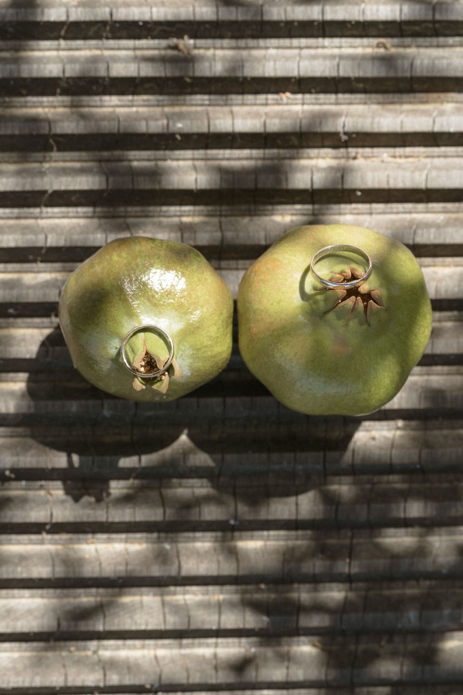Two fresh green pomegranates on a striped surface casting dramatic shadows.