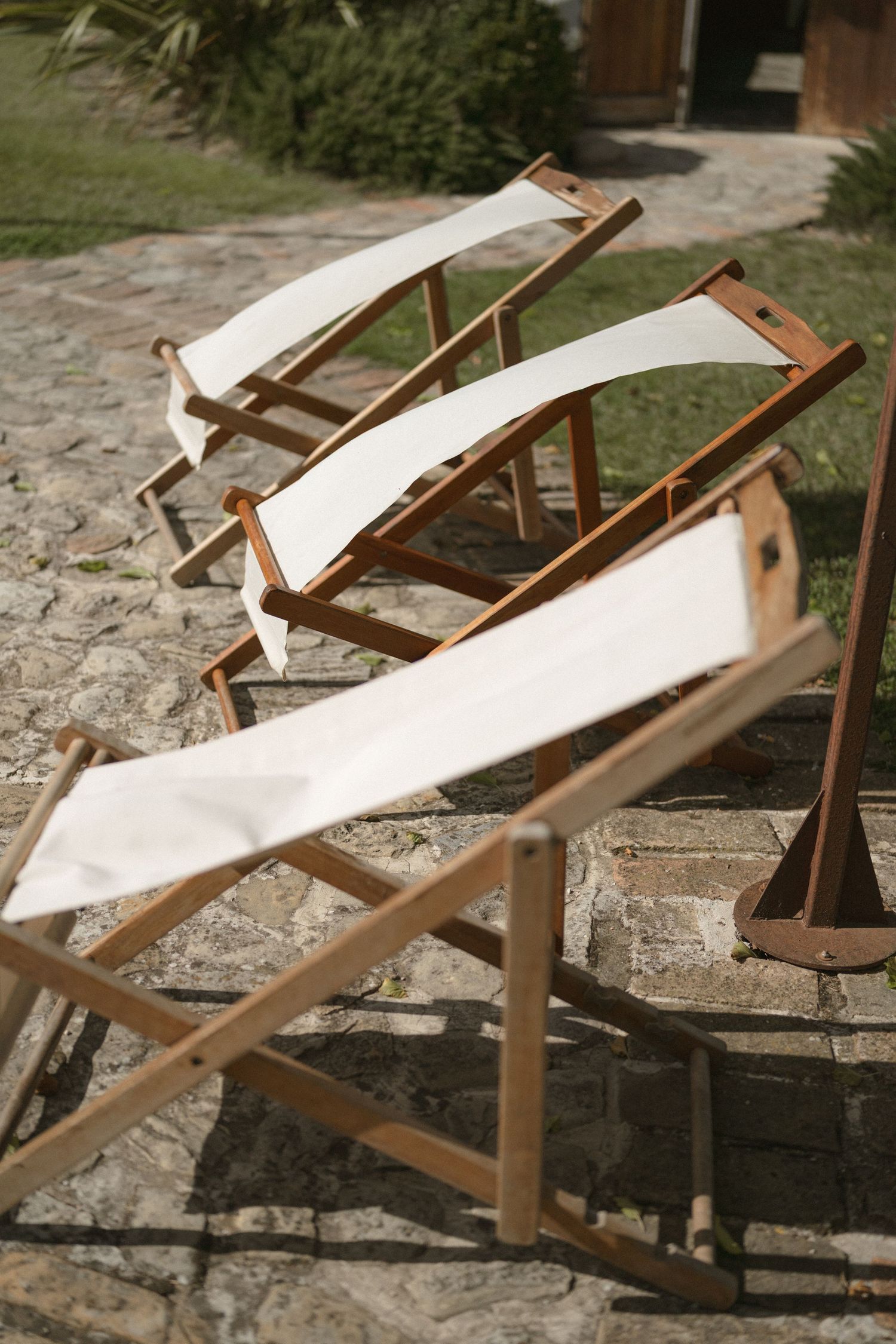 A sequence of five photos showing wooden beach chairs with white canvas seats arranged on stone pavement outdoors.