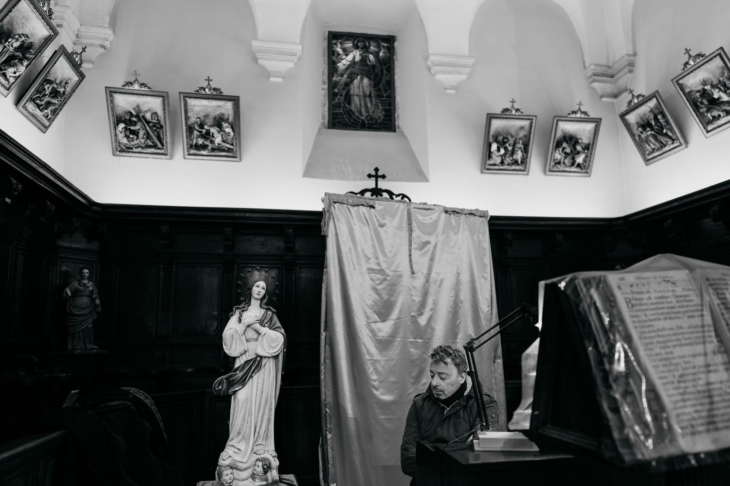 A musician plays piano in a historic church interior adorned with religious paintings and a statue of Mary.