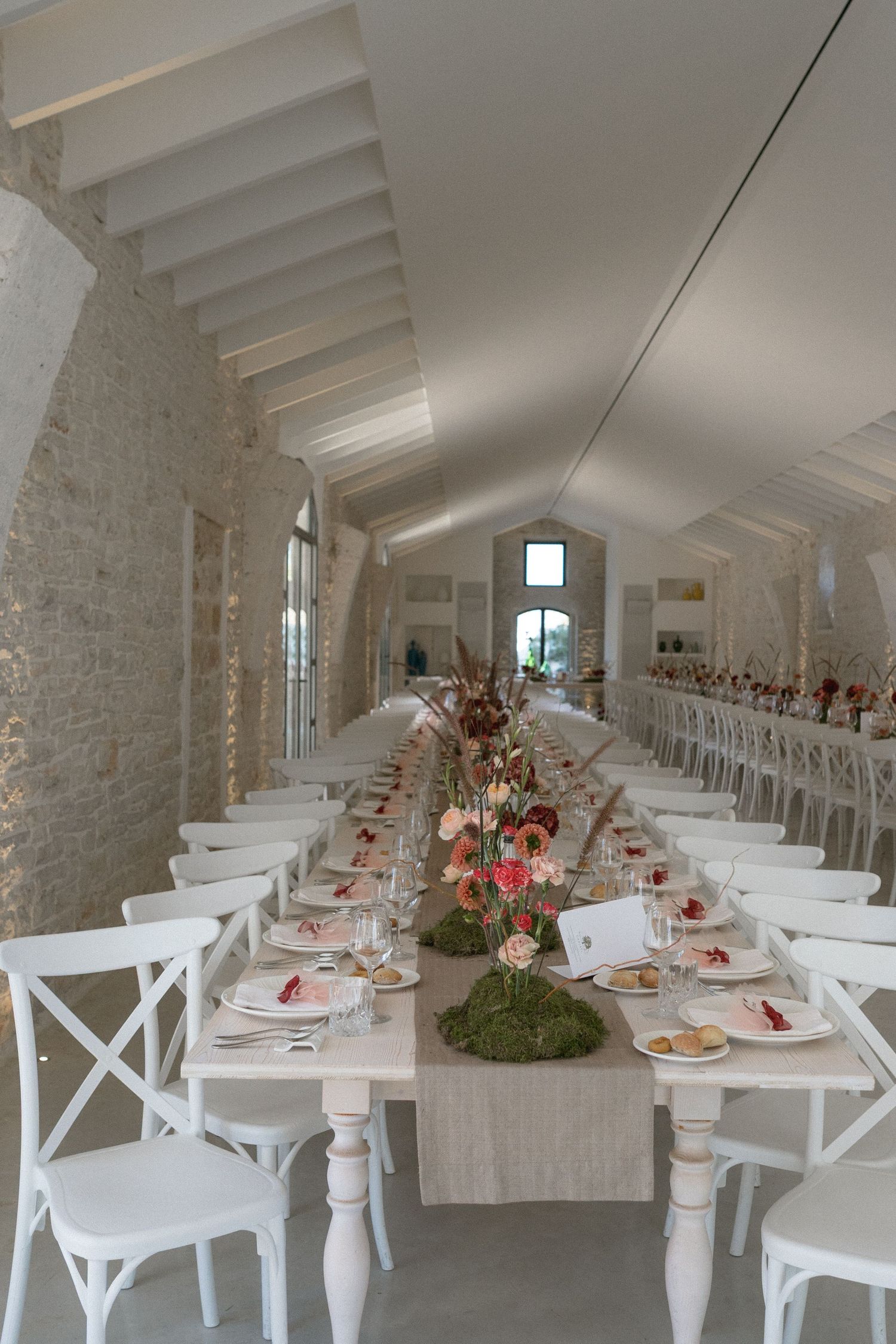 Elegant long wedding reception table with floral centerpieces in white vaulted stone venue.