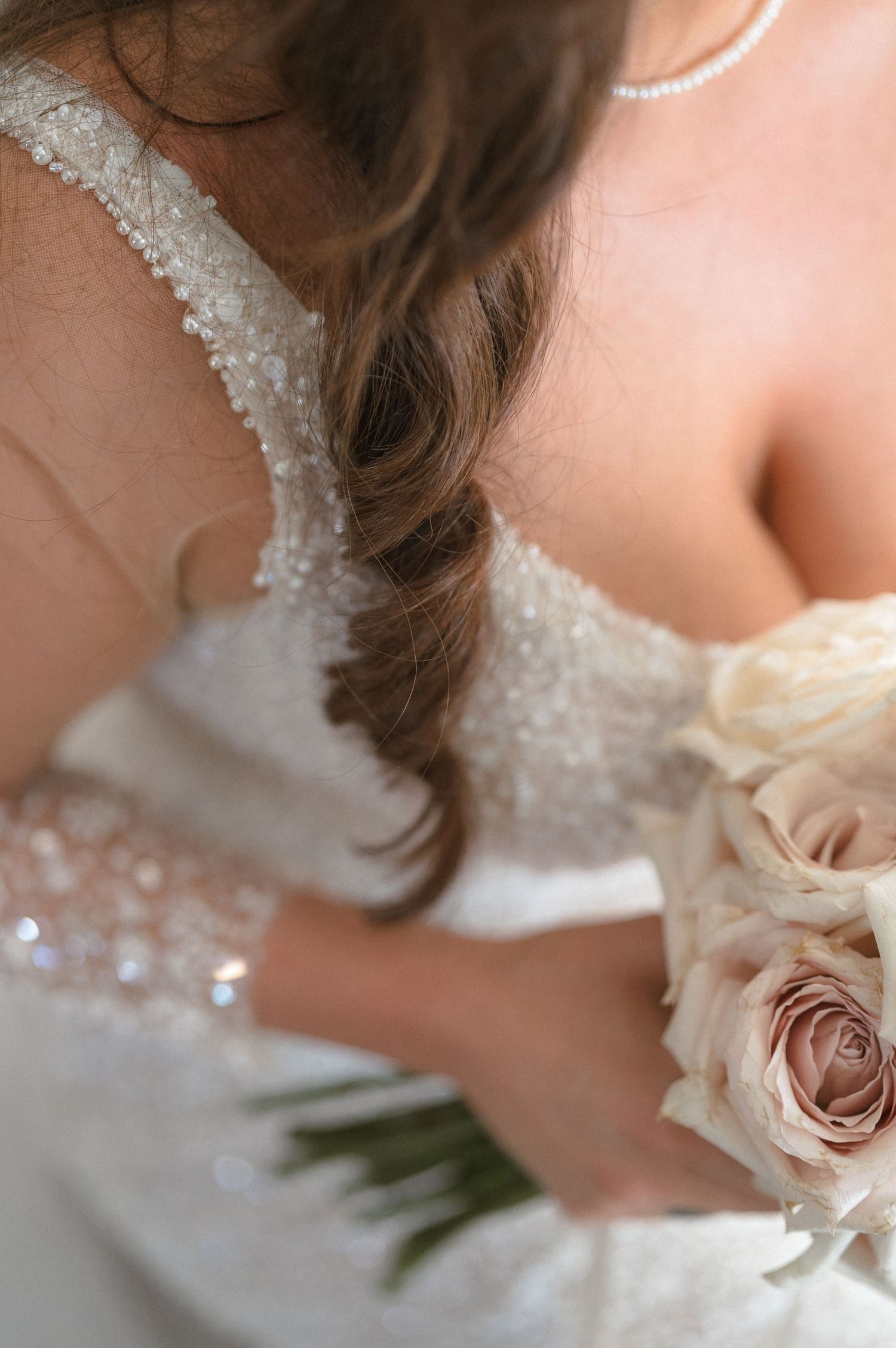 Close-up detail of a delicate blush pink rose against white lace wedding dress fabric.