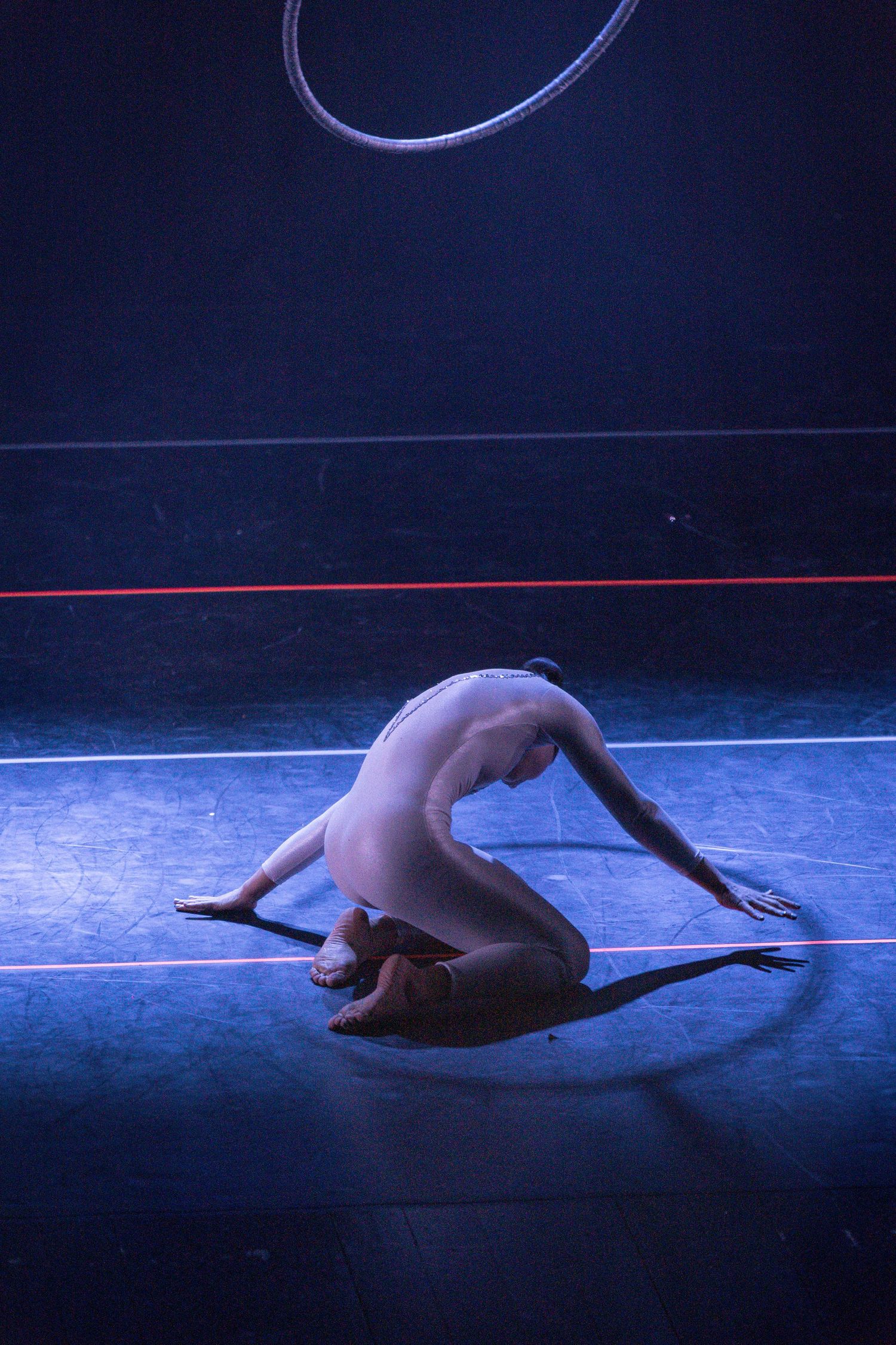 A dancer performs a graceful contemporary dance movement on a dark stage illuminated by blue lighting.