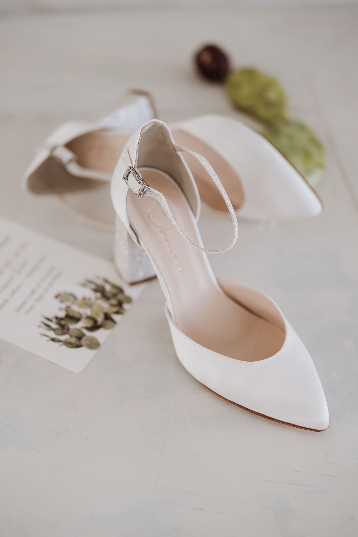Elegant white bridal shoe with ankle strap displayed on a light surface.